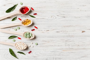 Renkli arka planda tahta kaşıkta vitamin ve mineral haplarının üst görünümü. Muhtelif ilaç haplarının en üst görüntüsü. Beslenme takviyesi sağlık ürünleri.
