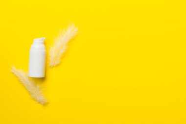 Pembe pastel arka planda, devekuşu tüyleriyle cilt bakımı serumları. Spa kozmetik ürünü, krem kavanozu, markalaşma modeli, fotokopi alanı olan üst görünüm.