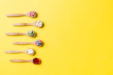 Renkli arka planda tahta kaşıkta vitamin ve mineral haplarının üst görünümü. Muhtelif ilaç haplarının en üst görüntüsü. Beslenme takviyesi sağlık ürünleri.