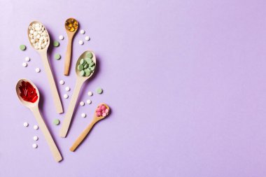Renkli arka planda tahta kaşıkta vitamin ve mineral haplarının üst görünümü. Muhtelif ilaç haplarının en üst görüntüsü. Beslenme takviyesi sağlık ürünleri.
