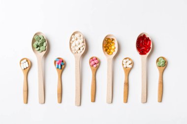 Renkli arka planda tahta kaşıkta vitamin ve mineral haplarının üst görünümü. Muhtelif ilaç haplarının en üst görüntüsü. Beslenme takviyesi sağlık ürünleri.