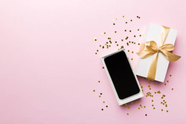 Altın kurdeleli hediye kutusu ve arka planda akıllı telefon, üst manzara. Boş kutu paketleme modeli, tasarımınız için şablon - markalaşma modeli.