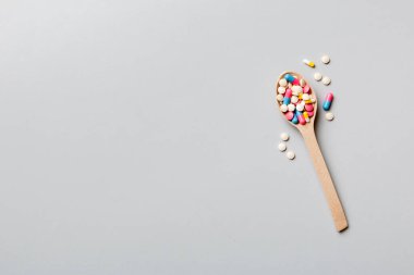 Renkli bir arka planda tahta kaşıkta vitamin kapsülleri. Haplar sağlıklı bir yemek olarak sunuldu. Uyuşturucu, eczane, ilaç veya sağlık hizmetleri kavramı.