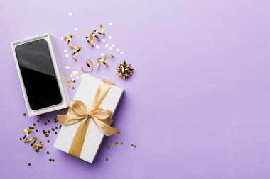 Altın kurdeleli hediye kutusu ve arka planda akıllı telefon, üst manzara. Boş kutu paketleme modeli, tasarımınız için şablon - markalaşma modeli.
