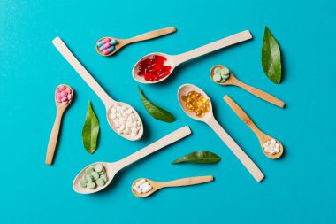 Renkli arka planda tahta kaşıkta vitamin ve mineral haplarının üst görünümü. Muhtelif ilaç haplarının en üst görüntüsü. Beslenme takviyesi sağlık ürünleri.