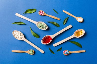 Renkli arka planda tahta kaşıkta vitamin ve mineral haplarının üst görünümü. Muhtelif ilaç haplarının en üst görüntüsü. Beslenme takviyesi sağlık ürünleri.