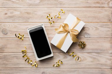 Altın kurdeleli hediye kutusu ve arka planda akıllı telefon, üst manzara. Boş kutu paketleme modeli, tasarımınız için şablon - markalaşma modeli.