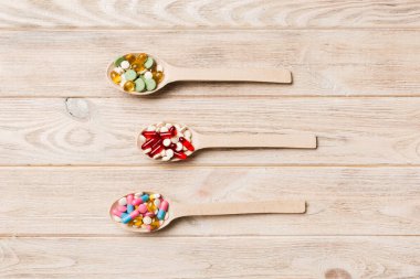 Renkli bir arka planda tahta kaşıkta vitamin kapsülleri. Haplar sağlıklı bir yemek olarak sunuldu. Uyuşturucu, eczane, ilaç veya sağlık hizmetleri kavramı.