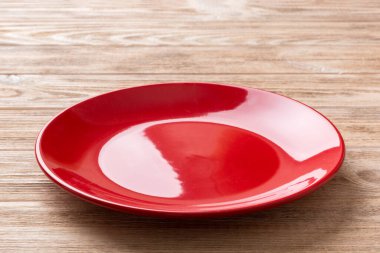 Ahşap zemindeki boş kırmızı tabağın perspektif görüntüsü. Tasarımın için boş boşluk.