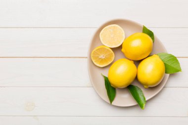 Taze kesilmiş limon ve tüm limonları renkli arka planda yuvarlak tabakta. Yemek ve içecek malzemeleri hazırlanıyor. Sağlıklı beslenme teması üst görünüm kopyalama alanı.