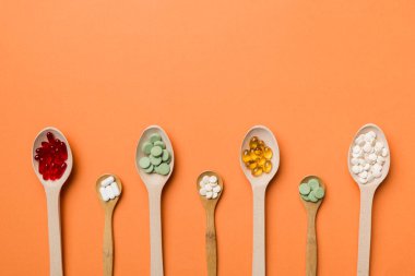 Renkli arka planda tahta kaşıkta vitamin ve mineral haplarının üst görünümü. Muhtelif ilaç haplarının en üst görüntüsü. Beslenme takviyesi sağlık ürünleri.