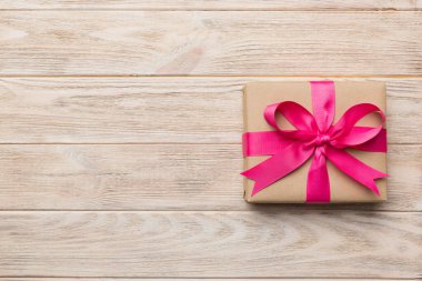 El işi kağıdına sarılı, masa arkasında renkli bir fiyonk olan tatil hediyesi kutusu. Üst görünüm, düz görünüm, kopyalama alanı.