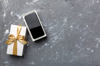 Altın kurdeleli hediye kutusu ve arka planda akıllı telefon, üst manzara. Boş kutu paketleme modeli, tasarımınız için şablon - markalaşma modeli.