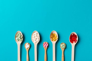Renkli arka planda tahta kaşıkta vitamin ve mineral haplarının üst görünümü. Muhtelif ilaç haplarının en üst görüntüsü. Beslenme takviyesi sağlık ürünleri.