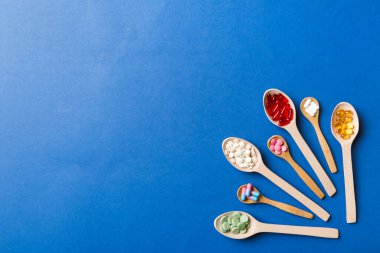 Renkli arka planda tahta kaşıkta vitamin ve mineral haplarının üst görünümü. Muhtelif ilaç haplarının en üst görüntüsü. Beslenme takviyesi sağlık ürünleri.