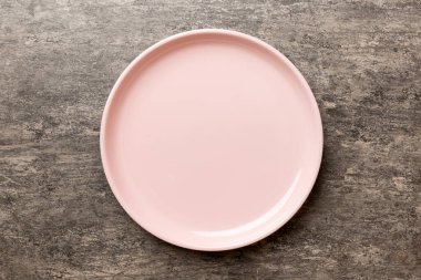 Çimento arka planındaki boş pembe tabağın üst görüntüsü. Tasarımın için boş boşluk.