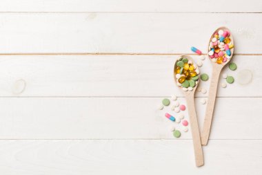 Renkli bir arka planda tahta kaşıkta vitamin kapsülleri. Haplar sağlıklı bir yemek olarak sunuldu. Uyuşturucu, eczane, ilaç veya sağlık hizmetleri kavramı.