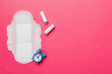 Alarm saatini hijyenik kadın tamponları ve regl pedleri ile çalıyor. Tıbbi konsept kadın kritik günler ve regl dönemi. Kadın günlük hijyen. Boşluğu kopyala.