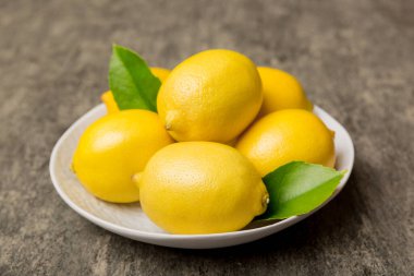Taze kesilmiş limon ve tüm limonları renkli arka planda yuvarlak tabakta. Yemek ve içecek malzemeleri hazırlanıyor. Sağlıklı beslenme teması üst görünüm kopyalama alanı.