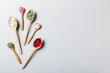 Renkli arka planda tahta kaşıkta vitamin ve mineral haplarının üst görünümü. Muhtelif ilaç haplarının en üst görüntüsü. Beslenme takviyesi sağlık ürünleri.