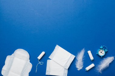 Alarm saatini hijyenik kadın tamponları ve regl pedleri ile çalıyor. Tıbbi konsept kadın kritik günler ve regl dönemi. Kadın günlük hijyen. Boşluğu kopyala.