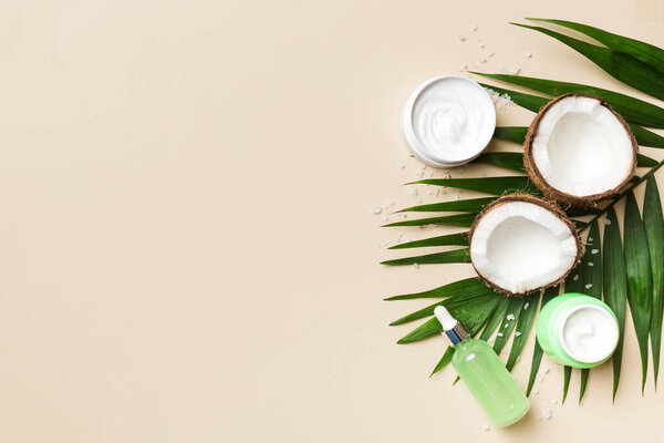 Coconut with jars of coconut oil and cosmetic cream on colored background. Top view. Free space for your text. Natural spa coconut cosmetics and organic treatment concept Coconut Spa composition.