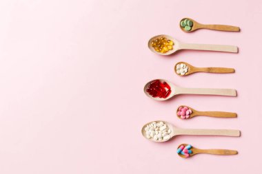 Renkli arka planda tahta kaşıkta vitamin ve mineral haplarının üst görünümü. Muhtelif ilaç haplarının en üst görüntüsü. Beslenme takviyesi sağlık ürünleri.