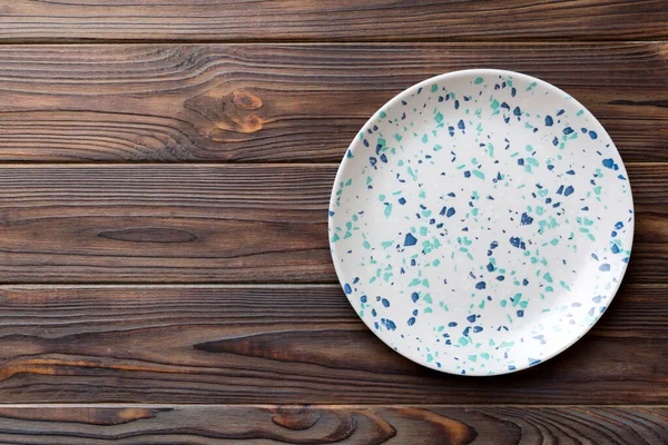 Ahşap zemindeki boş renkli tabağın üst görünümü. Tasarımın için boş boşluk.