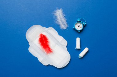 Alarm saatini hijyenik kadın tamponları ve regl pedleri ile çalıyor. Tıbbi konsept kadın kritik günler ve regl dönemi. Kadın günlük hijyen. Boşluğu kopyala.