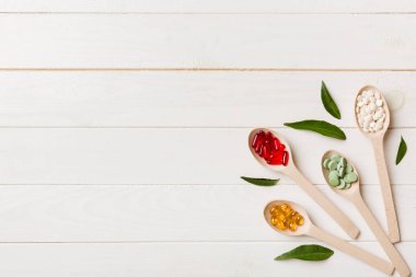 Renkli arka planda tahta kaşıkta vitamin ve mineral haplarının üst görünümü. Muhtelif ilaç haplarının en üst görüntüsü. Beslenme takviyesi sağlık ürünleri.