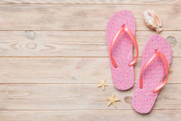 Renkli arka planda parmak arası terlikleri ve deniz kabuğu olan düz bir kompozisyon. Metin üstü görünümü için boşluk.