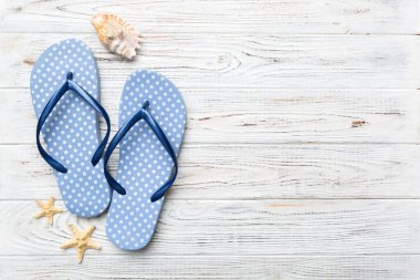 Renkli arka planda parmak arası terlikleri ve deniz kabuğu olan düz bir kompozisyon. Metin üstü görünümü için boşluk.