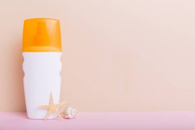 Plaj aksesuarları. Yazın UVB cilt koruması için nemlendirici güneş kremi şişesi ve renkli arka planda deniz kabukları. Kopyalama alanı kullan.