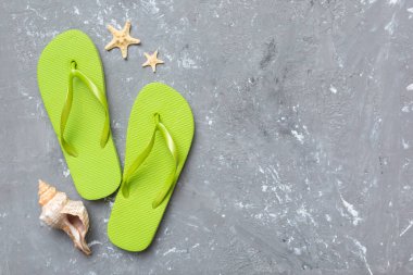 Renkli arka planda parmak arası terlikleri ve deniz kabuğu olan düz bir kompozisyon. Metin üstü görünümü için boşluk.