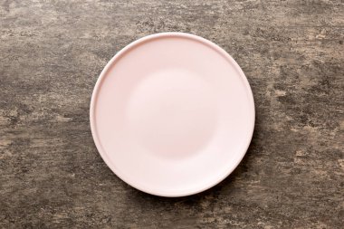 Çimento arka planındaki boş pembe tabağın üst görüntüsü. Tasarımın için boş boşluk.