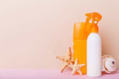 Plaj aksesuarları. Yazın UVB cilt koruması için nemlendirici güneş kremi şişesi ve renkli arka planda deniz kabukları. Kopyalama alanı kullan.