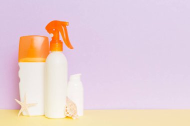 Plaj aksesuarları. Yazın UVB cilt koruması için nemlendirici güneş kremi şişesi ve renkli arka planda deniz kabukları. Kopyalama alanı kullan.