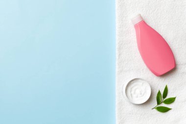Kozmetik şampuan şişesi renkli bir masada havluyla birlikte. Banyo arka planı, el ve vücut bakımı için tuvalet aksesuarları..
