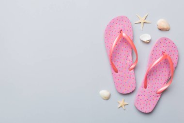 Renkli arka planda parmak arası terlikleri ve deniz kabuğu olan düz bir kompozisyon. Metin üstü görünümü için boşluk.