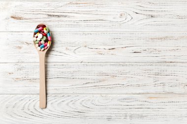 Renkli bir arka planda tahta kaşıkta vitamin kapsülleri. Haplar sağlıklı bir yemek olarak sunuldu. Uyuşturucu, eczane, ilaç veya sağlık hizmetleri kavramı.