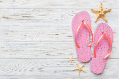 Renkli arka planda parmak arası terlikleri ve deniz kabuğu olan düz bir kompozisyon. Metin üstü görünümü için boşluk.