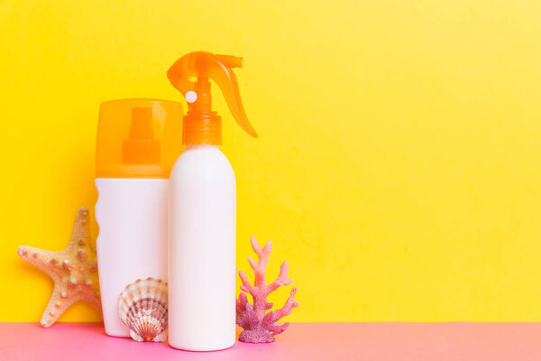 Beach accessories. Moisturiser sunscreen suntan lotion bottle for UVB skincare protection in summer with seashells on colored background. Mock up with copy space.