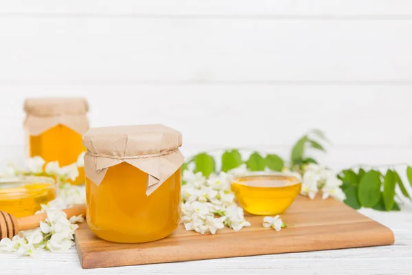 Sweet honey jar surrounded spring acacia blossoms. Honey flows from a spoon in a jar. jars of clear fresh acacia honey on wooden background.