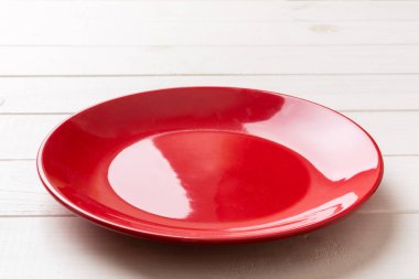 Ahşap zemindeki boş kırmızı tabağın perspektif görüntüsü. Tasarımın için boş boşluk.