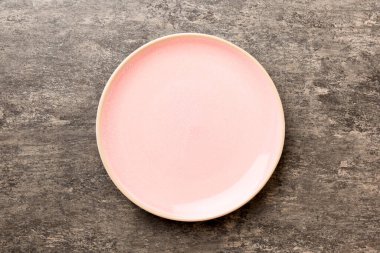 Çimento arka planındaki boş pembe tabağın üst görüntüsü. Tasarımın için boş boşluk.