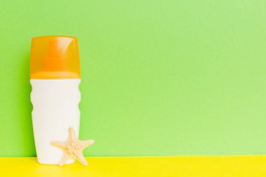 Plaj aksesuarları. Yazın UVB cilt koruması için nemlendirici güneş kremi şişesi ve renkli arka planda deniz kabukları. Kopyalama alanı kullan.