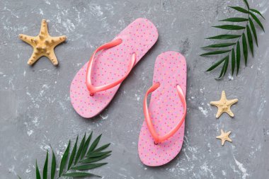 Renkli arka planda parmak arası terlikleri ve deniz kabuğu olan düz bir kompozisyon. Metin üstü görünümü için boşluk.