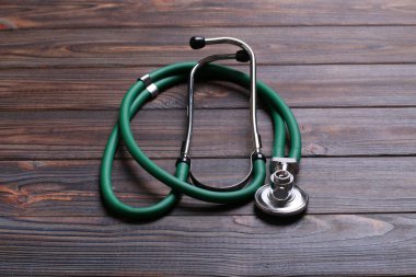 Koyu ahşap arka planda yeşil steteskopun üst görüntüsü. Tıbbi muayene kavramı.