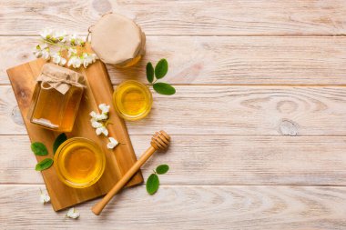 Akasya çiçekli bal kavanozu ve kesim tahtasında yapraklar. Taze bal üst görünüm düz yatıyordu.