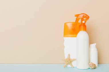 Plaj aksesuarları. Yazın UVB cilt koruması için nemlendirici güneş kremi şişesi ve renkli arka planda deniz kabukları. Kopyalama alanı kullan.
